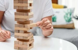 Midsection of woman sitting on sofa and playing jenga on white table.